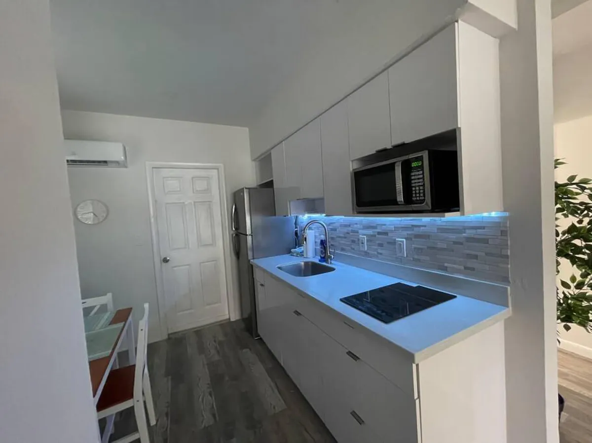 A modern kitchen space with a sleek countertop, built-in sink, glass cooktop, and microwave integrated above the counter. Adjacent to the kitchen is a dining table with chairs, all set within a clean, updated interior that encourages meal preparation and casual dining.